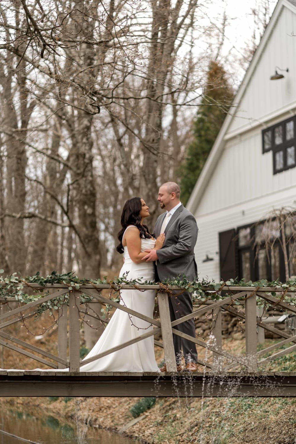 A bride and groom on a wooden footbridge among bare winter trees