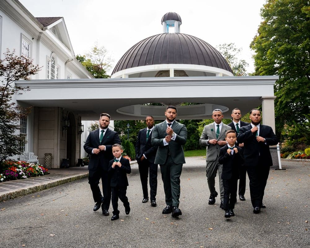 A groom, his groomsmen and two young ring bearers walking out from under a domed entrance canopy