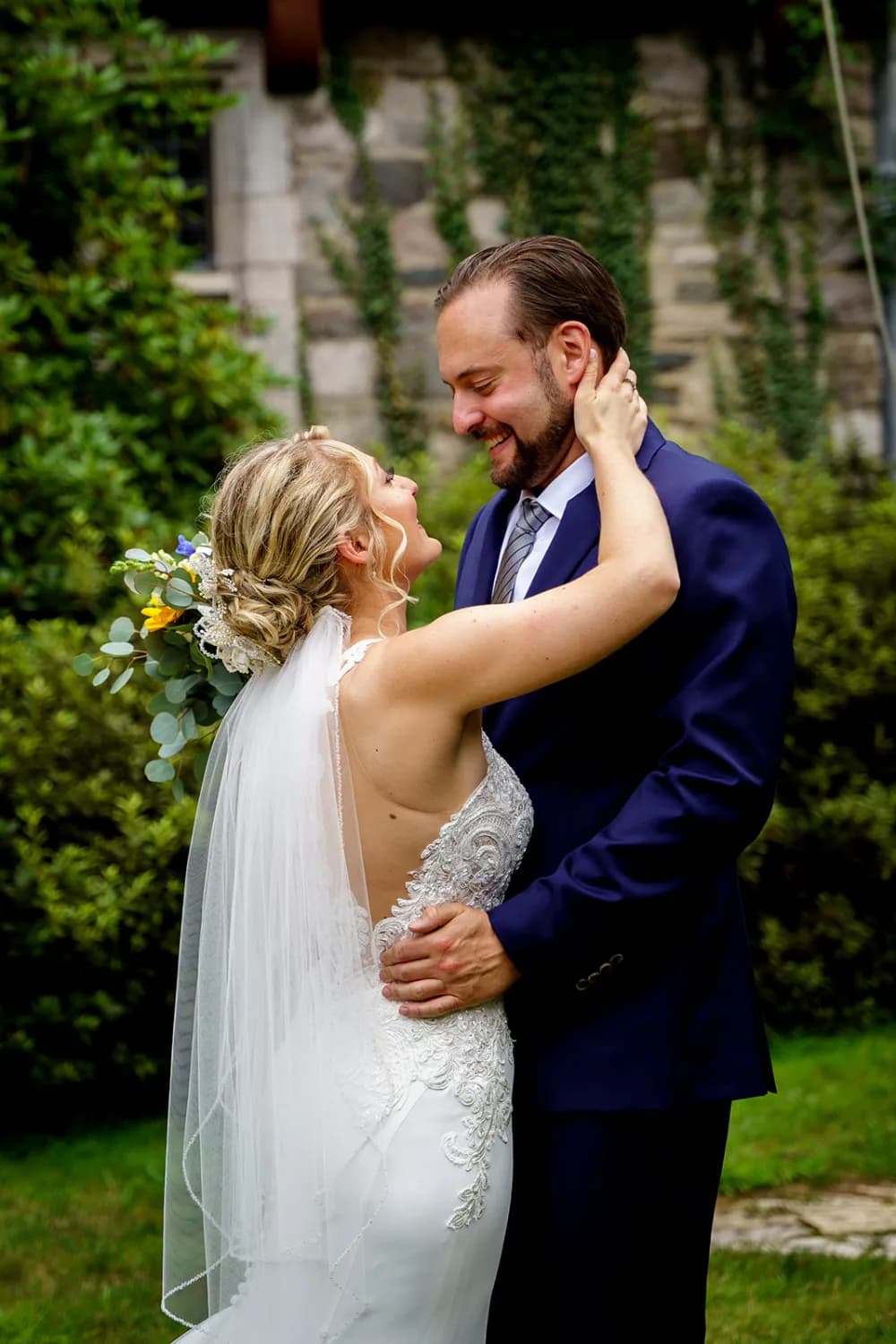A bride and groom embracing in a garden, both smiling