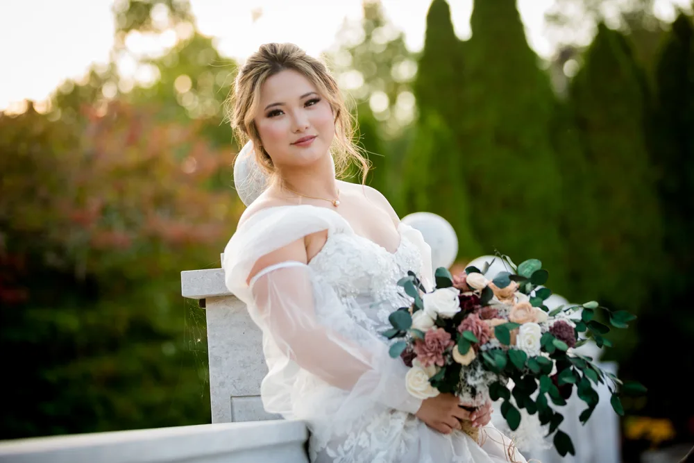 A bride holding her bouquet in late sun, autumn leaves behind her