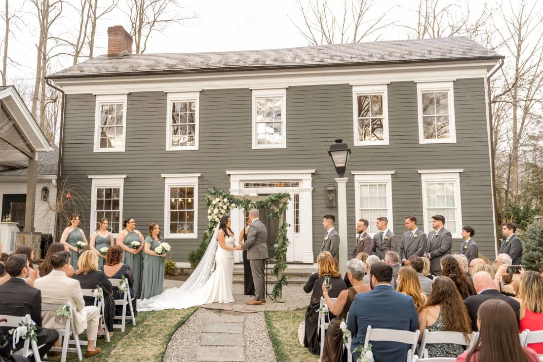 Jackie and Chris’s outdoor ceremony in front of a grey clapboard house at The Inn at Millrace Pond