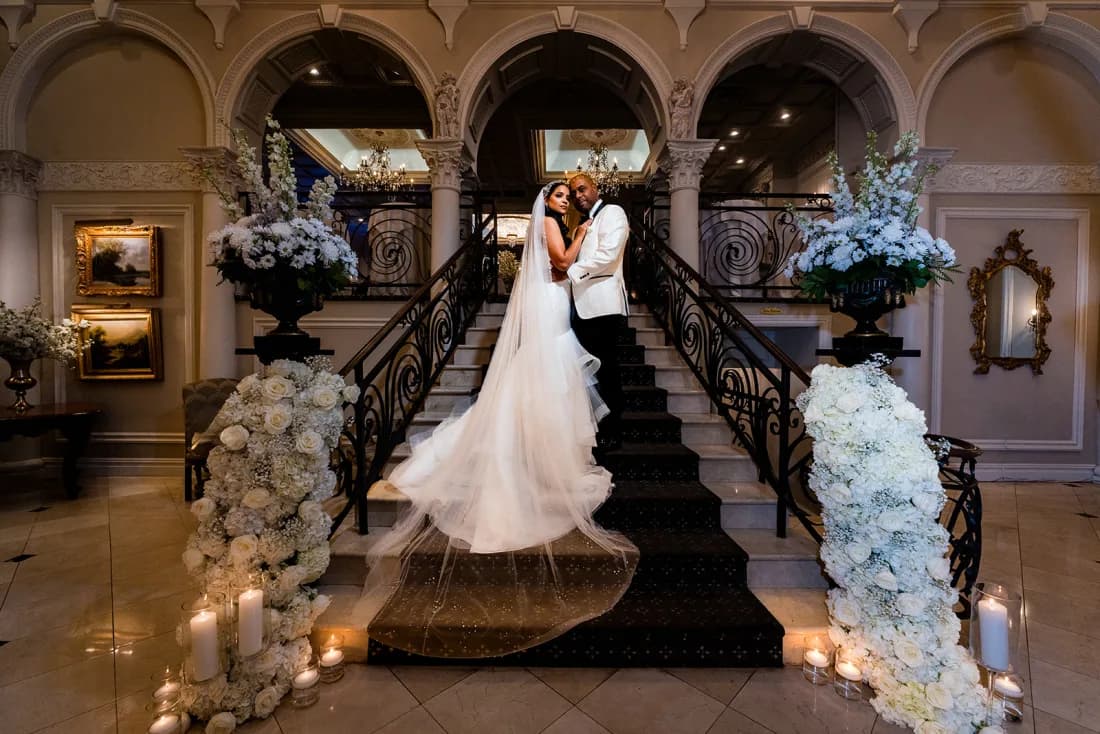 Judy and Mike at the foot of a flower-lined staircase beneath arched windows at Nanina’s In the Park