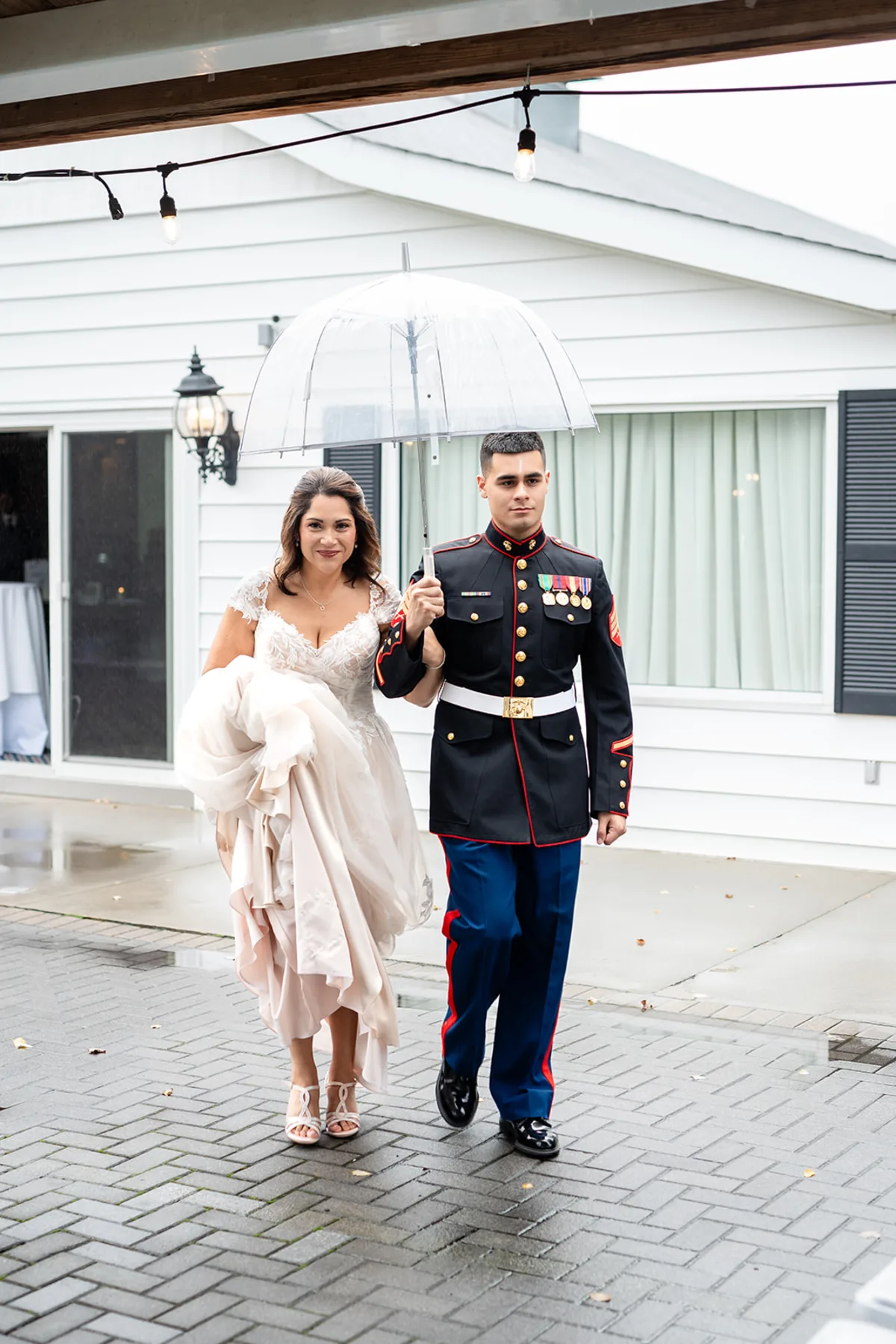 Bride and groom in Marine Corps dress blues walking under a clear umbrella outside the clubhouse at The Club at Picatinny