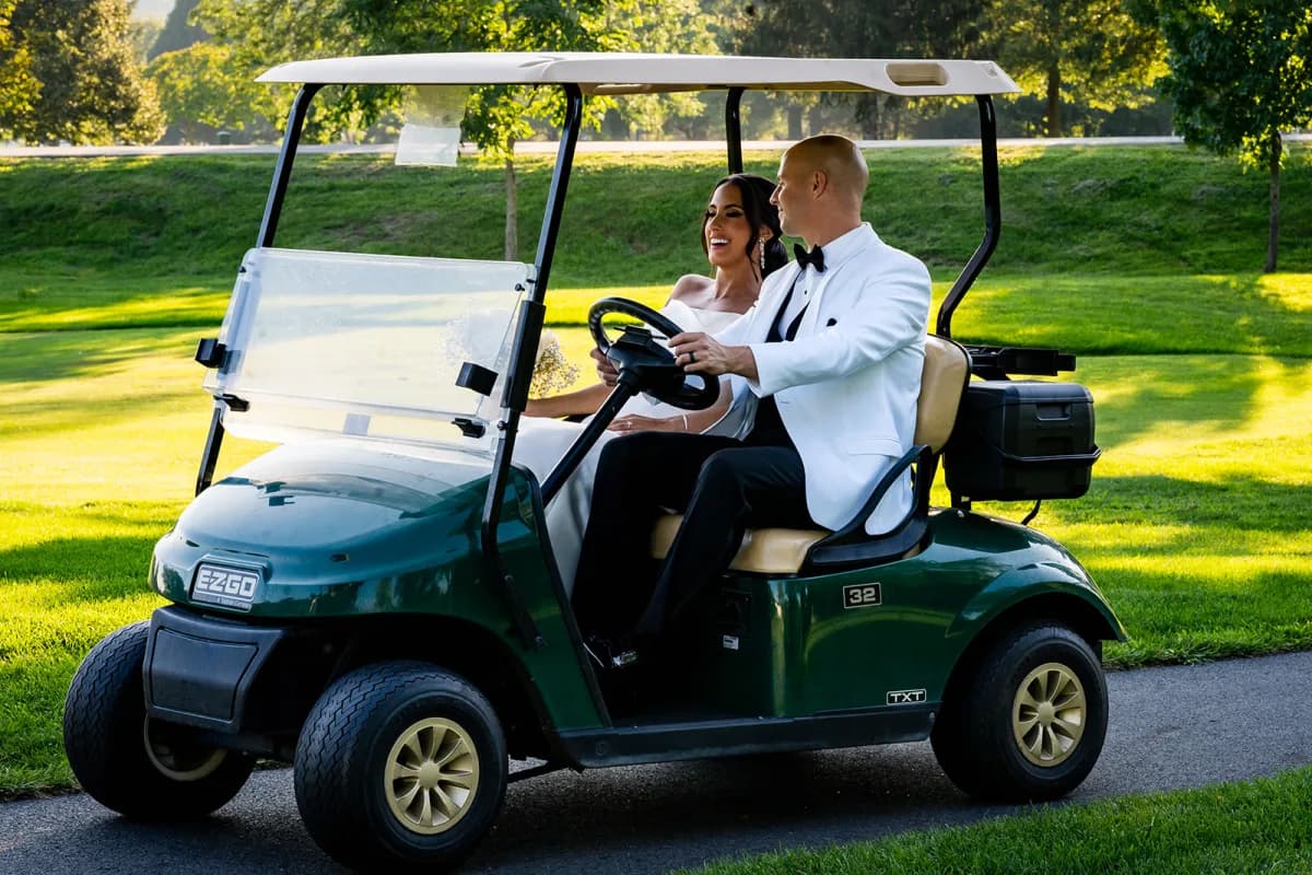 Bride and groom riding a golf cart across the course at The Club at Picatinny