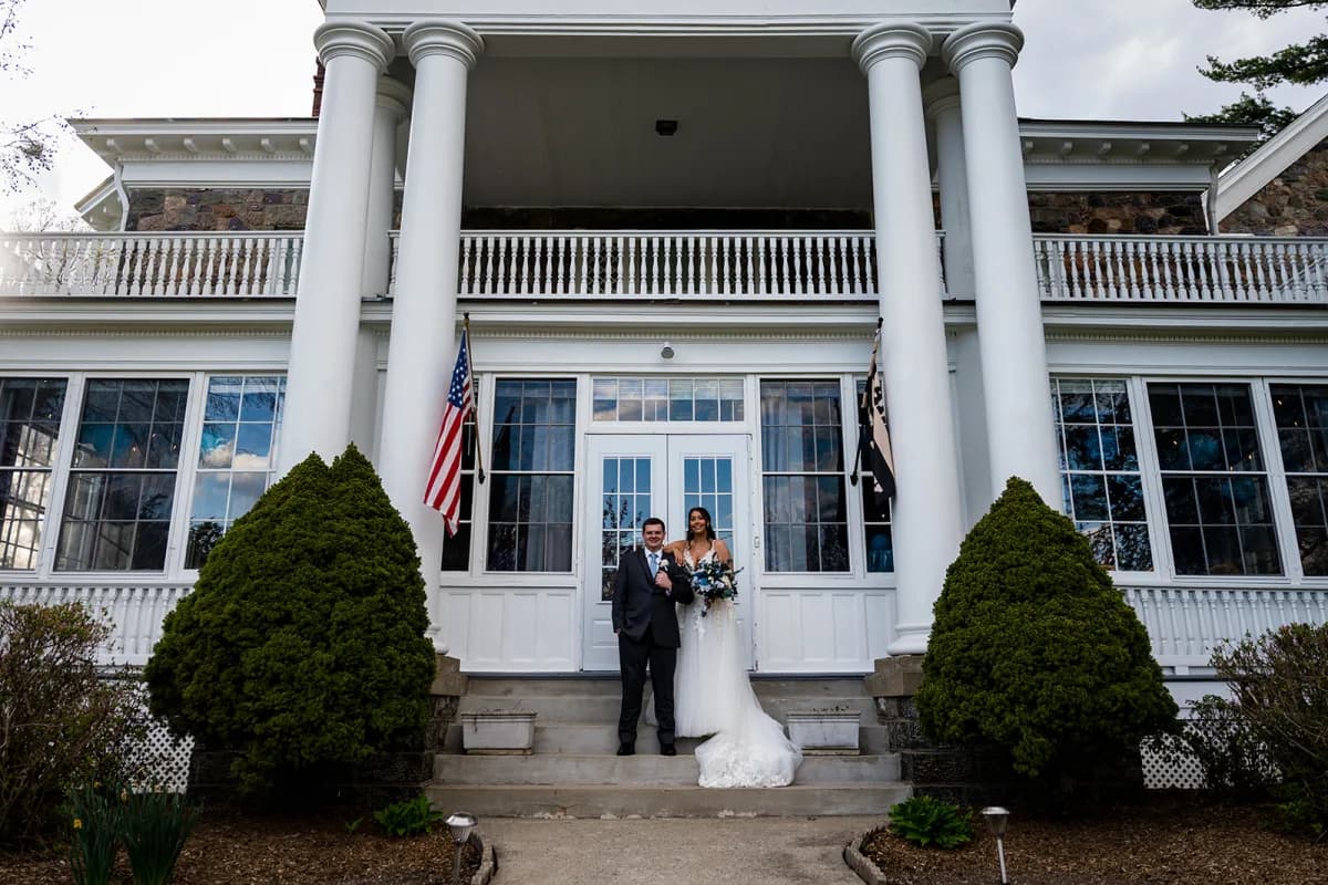 Couple between the white columns of the clubhouse entrance at The Club at Picatinny