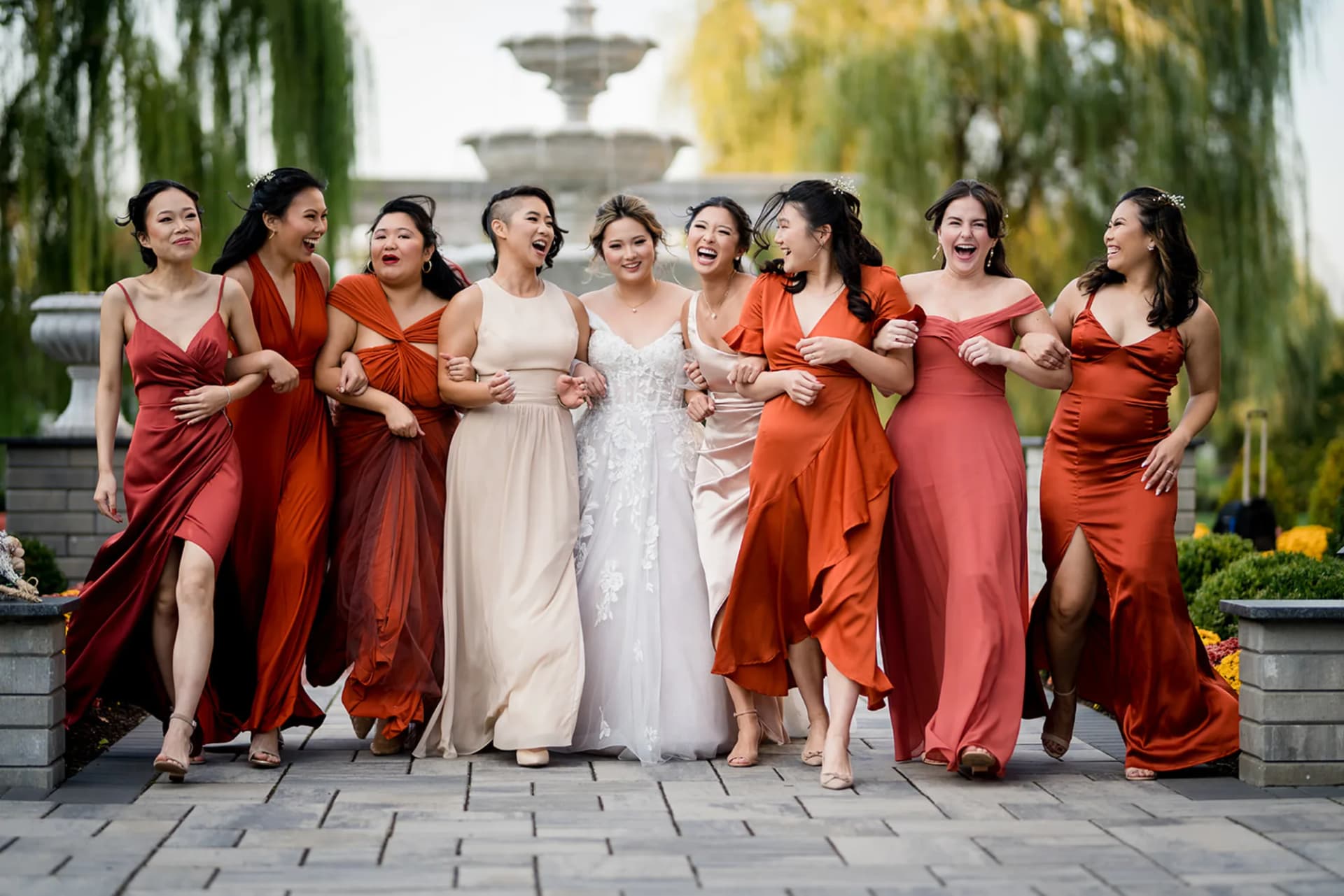 Amanda walking arm in arm with eight bridesmaids in rust and terracotta at The Mansion on Main Street