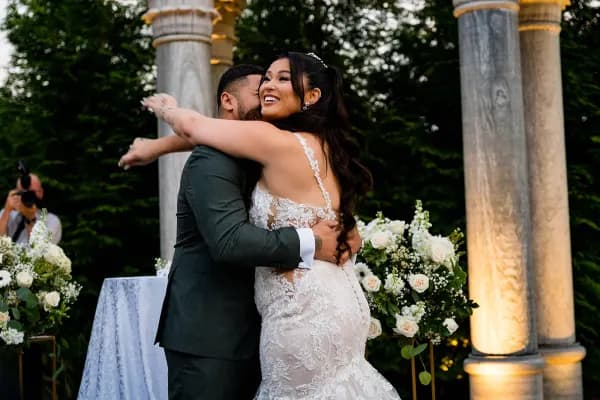 Anna and Jose hugging between stone columns at The Meadow Wood