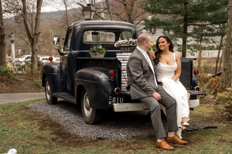 Jackie and Chris sitting on the tailgate of a vintage pickup truck at The Inn at Millrace Pond